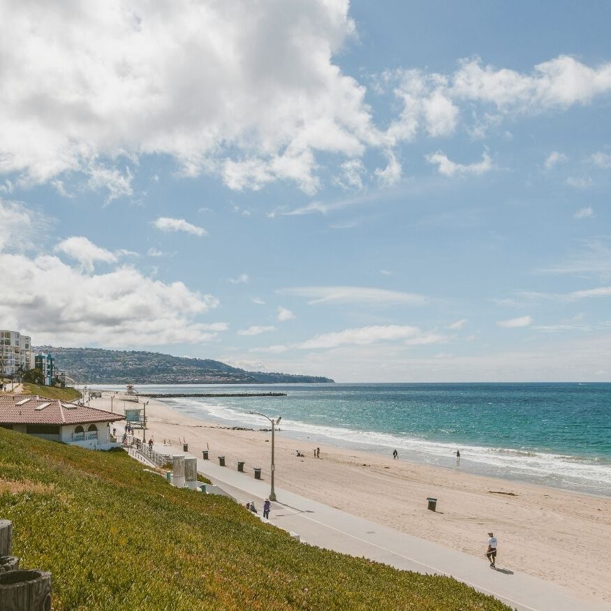 High-angle scenic view of a wide sandy beach and coastline in Southern California with white waves crashing and a clear horizon.